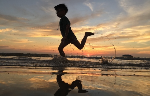 Маленький мальчик бежит по воде на закате