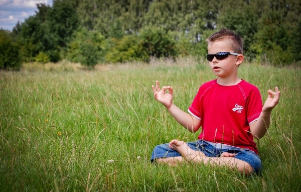 Маленький мальчик в очках медитирует на зеленой траве