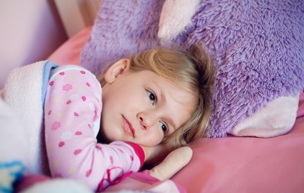 Маленькая кареглазая девочка лежит в кровати 