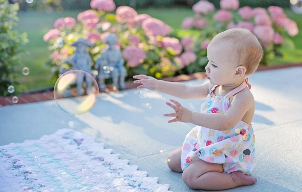 Маленькая девочка ловит мыльный пузырь