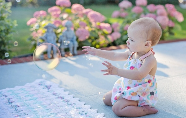 Маленькая девочка ловит мыльный пузырь на улице летом