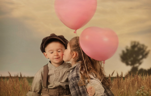 Маленькая девочка с шариками целует мальчика