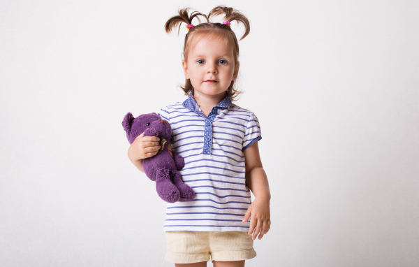 Маленькая девочка с игрушечным медведем на сером фоне