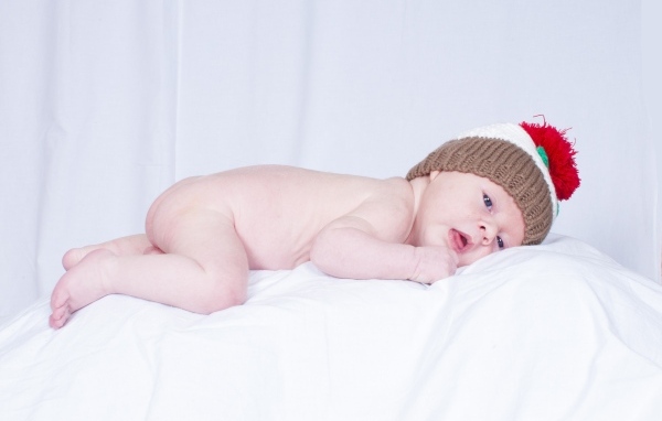 Новорожденный малыш в шапке на белой подушке
