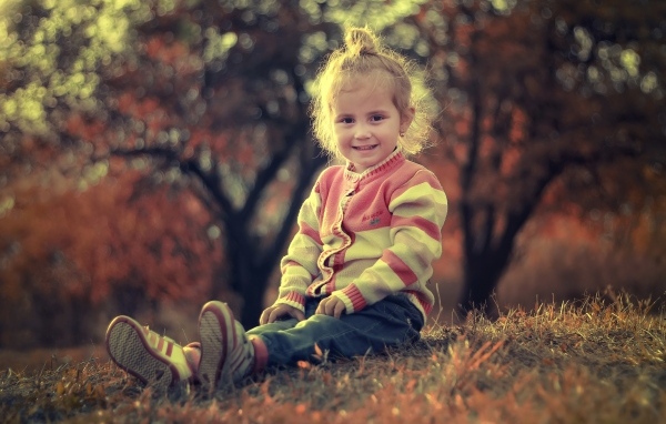 Настоящая маленькая девочка сидит на земле в лучах солнца