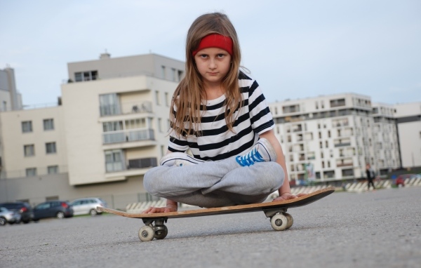 Серьезная девочка сидит на  скейтборде