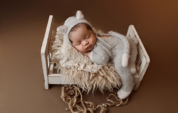 Спящий ребенок на маленькой кровати на коричневом фоне