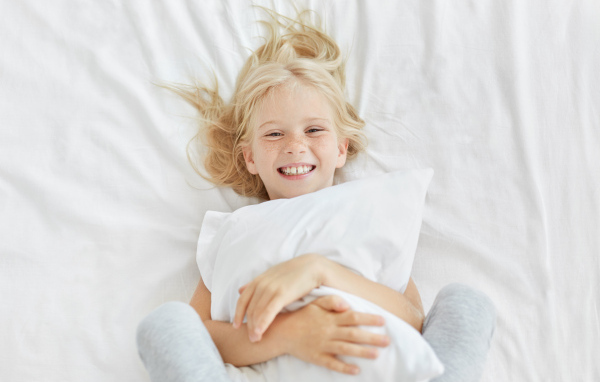 Улыбающаяся маленькая девочка с подушкой на кровати