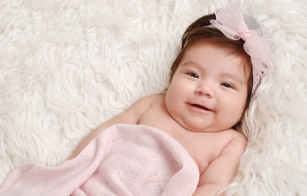 Улыбающаяся новорожденная малышка с бантом на голове