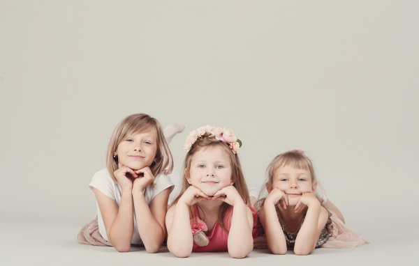 Три маленькие девочки лежат на сером фоне