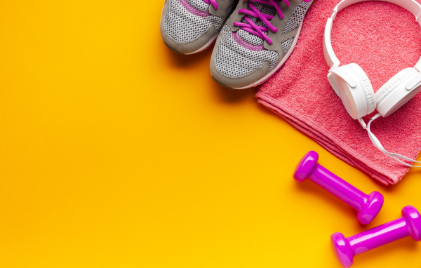 Розовые гантели, наушники, кроссовки и полотенце на желтом фоне