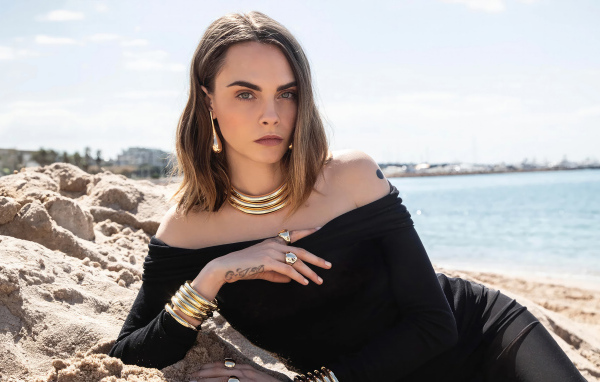 Кара Делевинь в черном платье лежит на песке