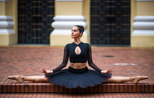 Девушка балерина в черном сидит на шпагате