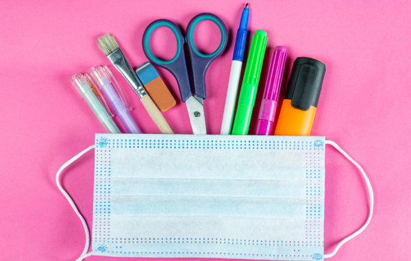 Канцелярские предметы и медицинская маска на розовом фоне