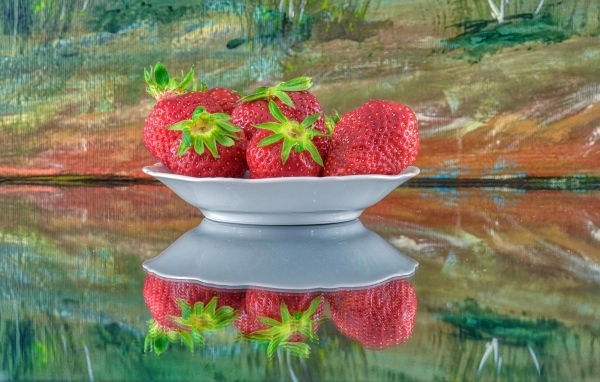 Белая тарелка с клубникой отражается в поверхности стола