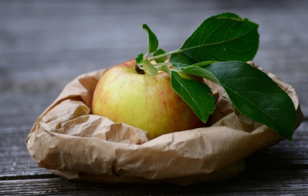 Яблоко с зелеными листьями на бумаге