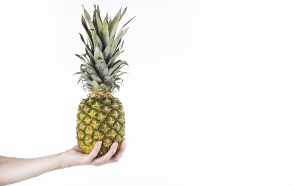 Большой ананас в руке на белом фоне