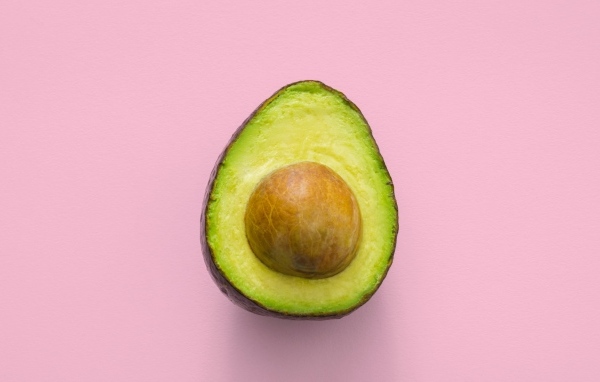 Половина авокадо с большой косточкой на розовом фоне