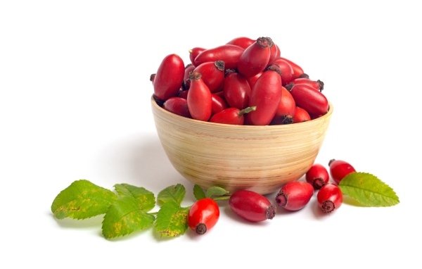 Тарелка с красными плодами шиповника на белом фоне
