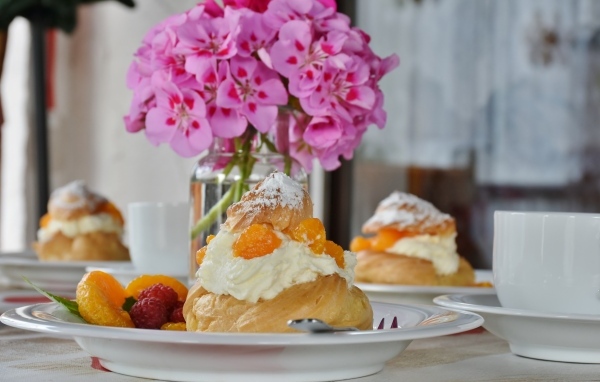 Булочки с кремом и фруктами на столе с букетом