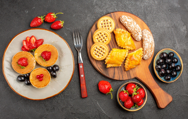 Печенье и оладьи на столе с ягодами клубники и виноградом