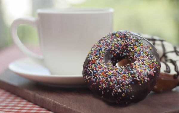 Донат с шоколадной глазурью и сладкой посыпкой на столе с чашкой чая