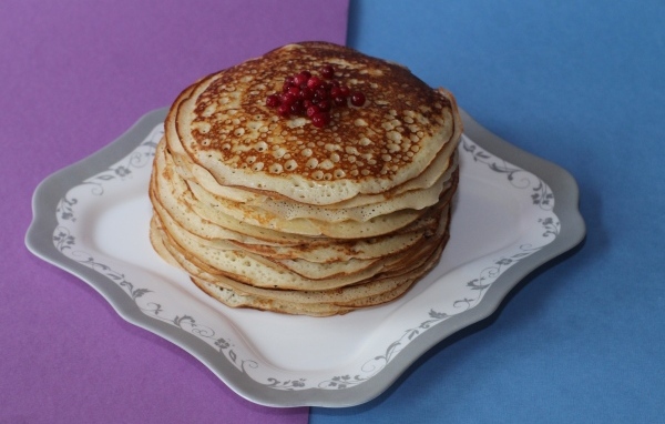 Тонкие блинчики с ягодами на большой тарелке на столе