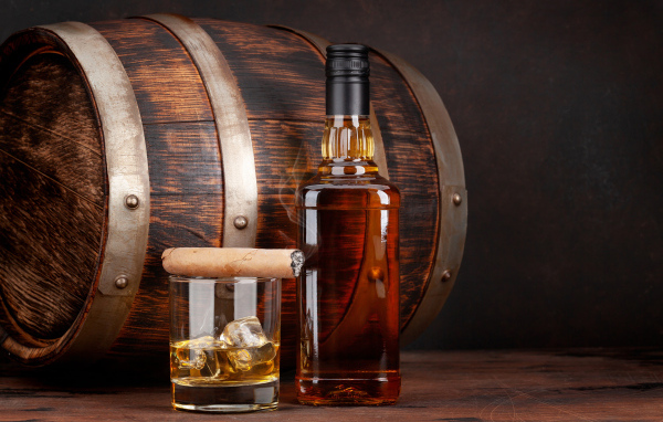 Бутылка виски на столе со стаканом, сигарой и бочкой