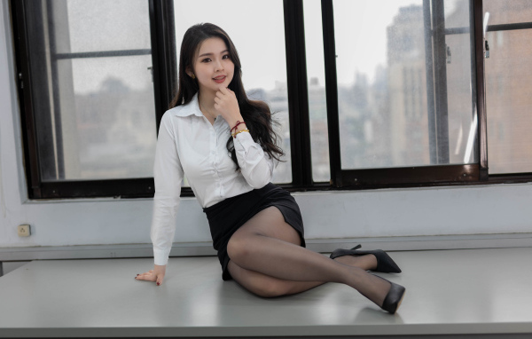 Девушка азиатка секретарь сидит на столе у окна