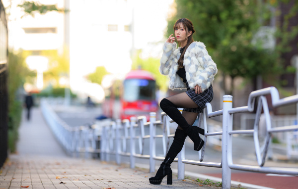 Азиатка в шубе стоит у забора