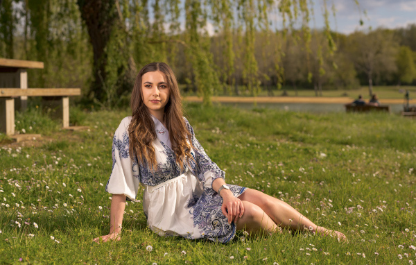 Красивая девушка в платье сидит на зеленой траве в парке