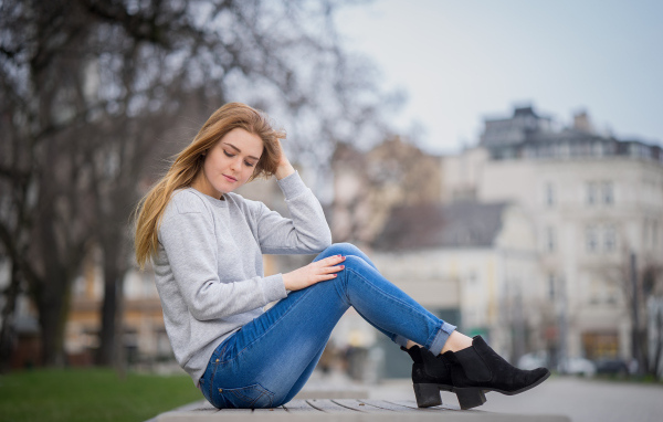 Милая девушка в синих джинсах сидит на лавке