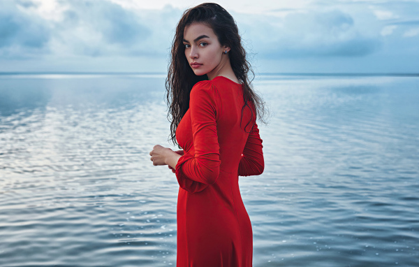 Милая девушка в красном платье стоит у воды