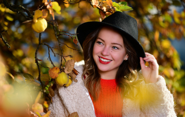 Улыбающаяся девушка в черной шляпе у дерева с яблоками