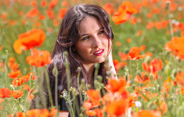 Молодая кареглазая девушка лежит на поле с красными маками