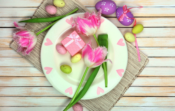 Пасхальные яйца с тюльпанами на тарелке на столе