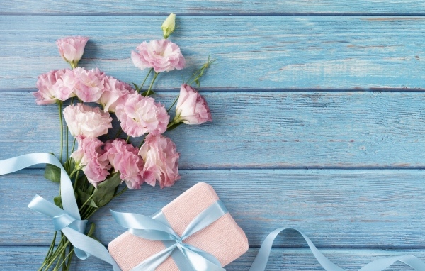 Букет розовых цветов эустомы с подарком на голубом столе