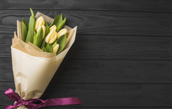 Букет желтых тюльпанов в бумаге на черном столе