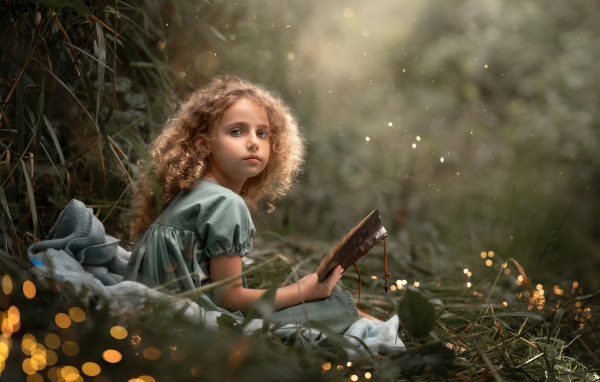 Милая девочка читает книгу сидя на траве