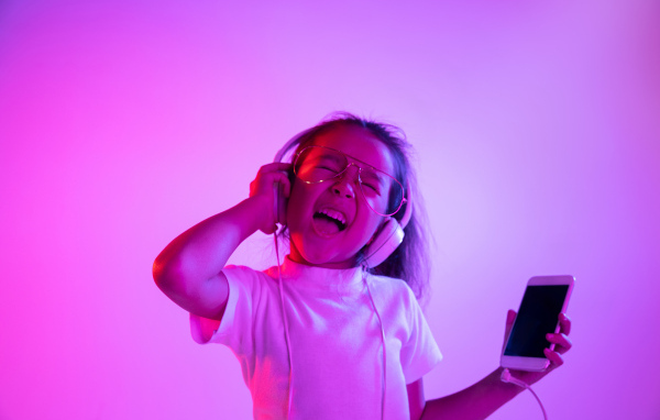 Маленькая девочка в наушниках с телефоном слушает музыку