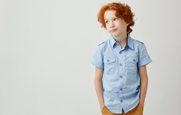 Рыжеволосый мальчик на фоне серой стены