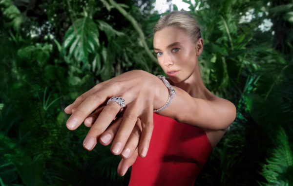 Актриса Ванесса Кирби в красном платье с кольцом на руке на фоне зарослей