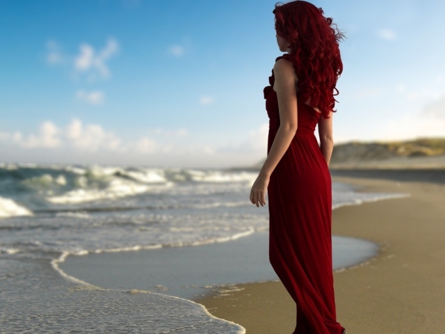 Girl with red hair in a red dress on the beach