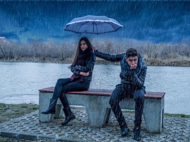 Парень держит над девушкой зонт во время дождя