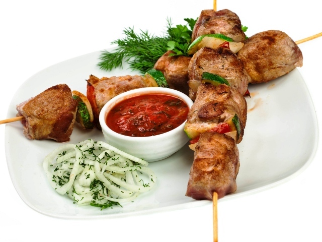 Skewers on a white plate with sauce, herbs and onions