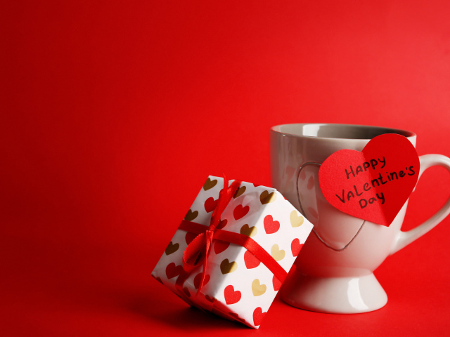 A cup with a gift and a valentine on a red background on February 14
