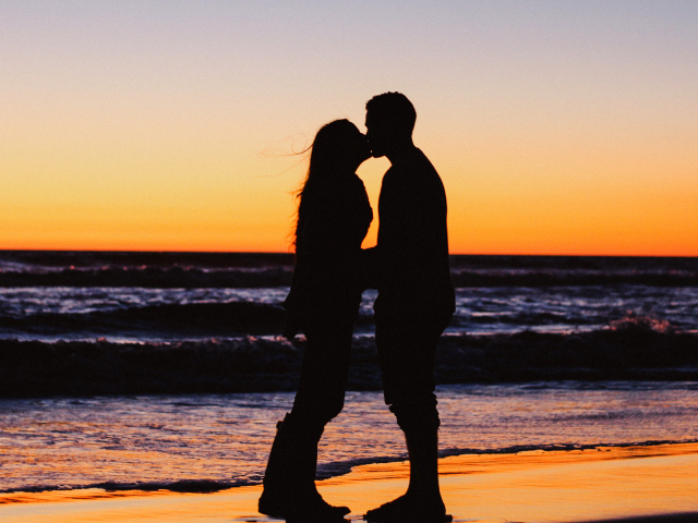 Поцелуй влюбленной пары на берегу моря на закате 