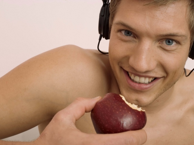 Handsome blue-eyed guy in headphones with an apple in his hand