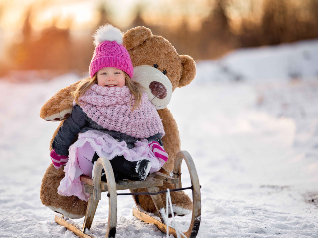 Маленькая девочка на санках с большим медведем зимой 