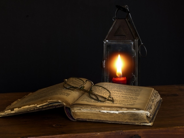 Старая книга с очками на столе со свечой 